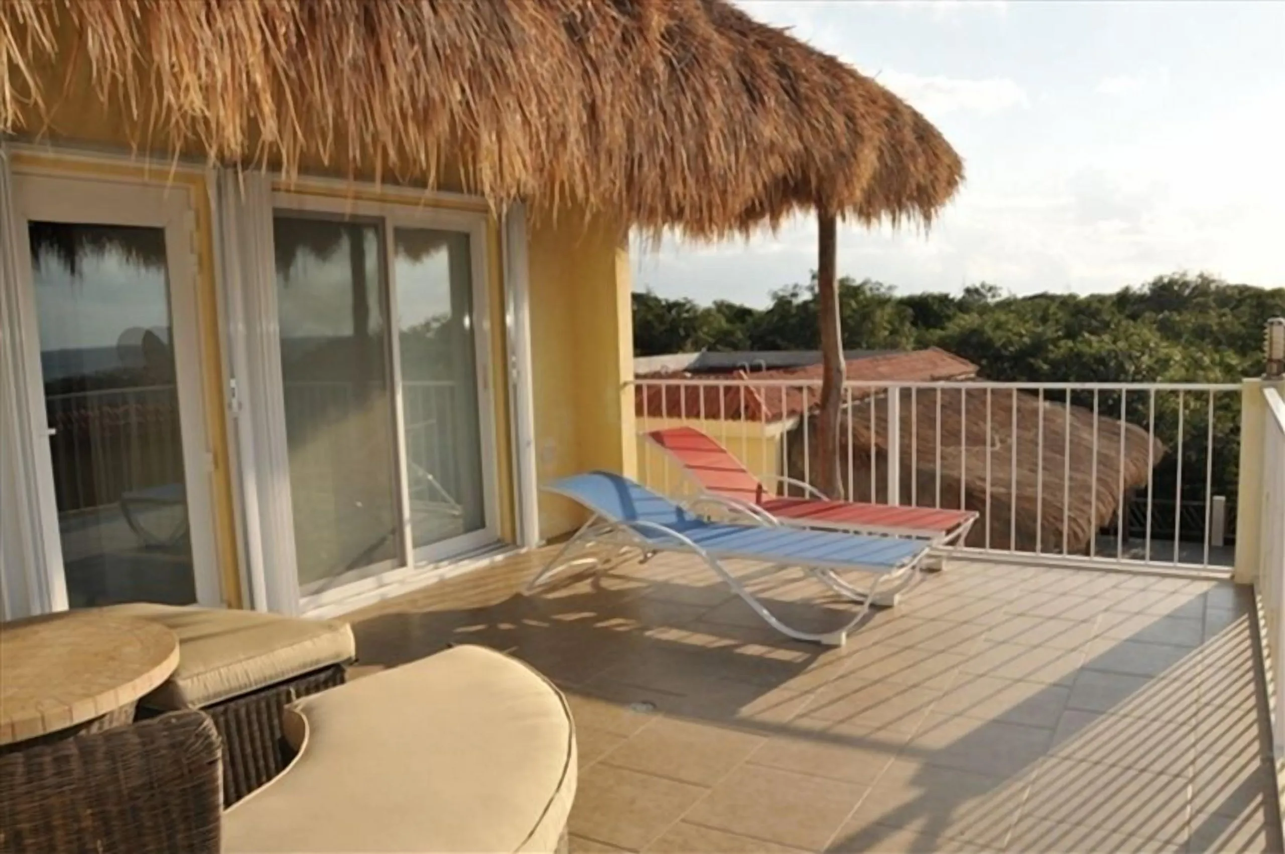 Second-floor balcony with palapa shade and sliding glass doors looking over the garden and jungle