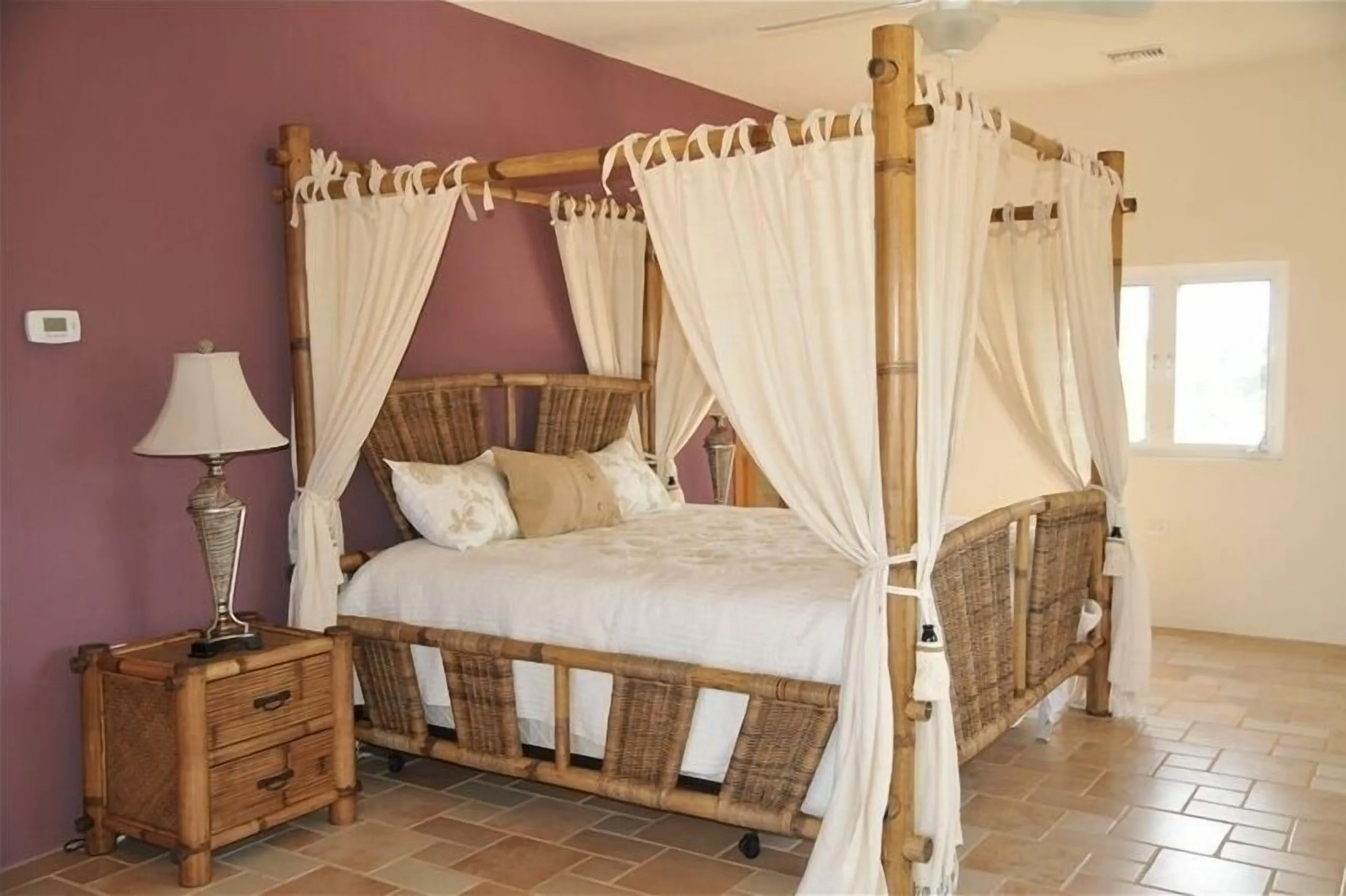 The Maui Room at Casa Dana with a white four-poster canopy king bed, bedside lamp and wicker chair