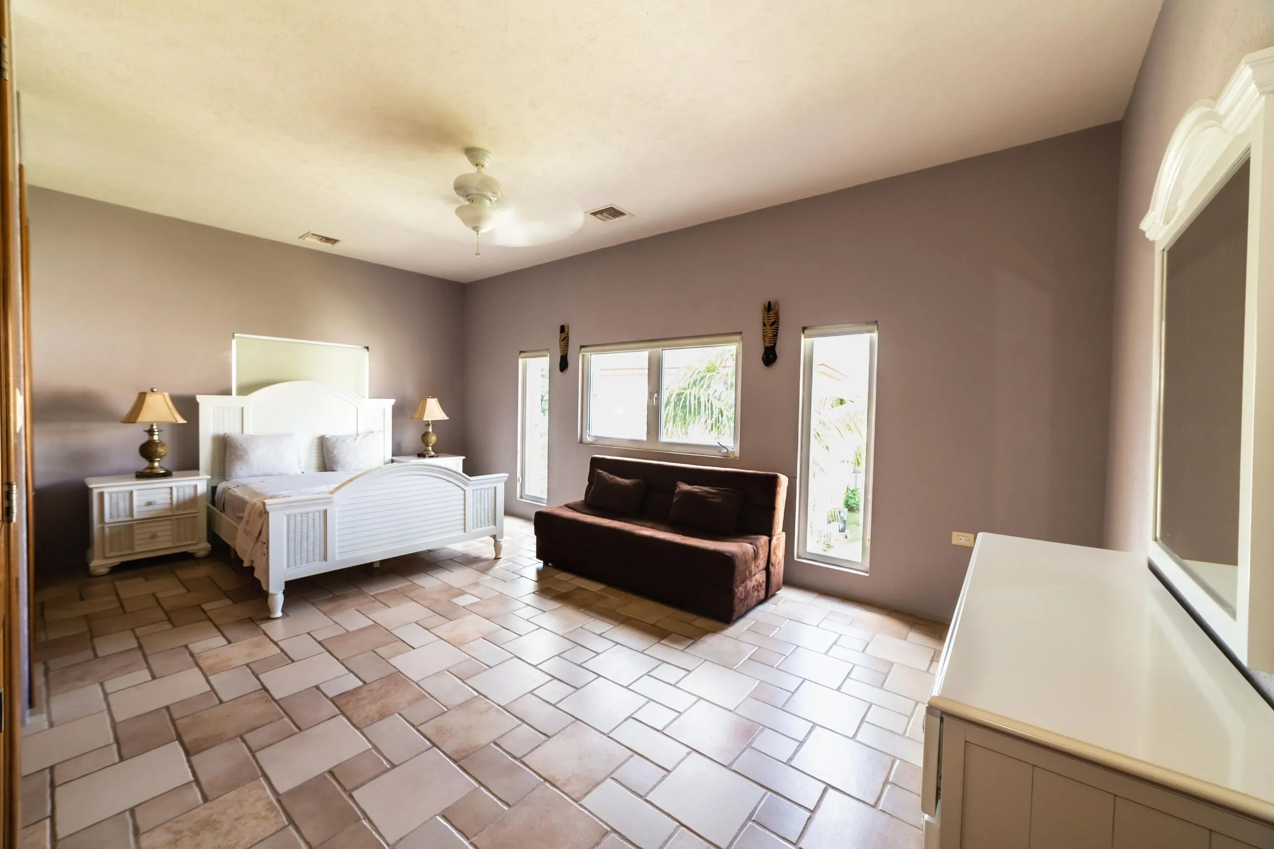 Bedroom with a made bed, nightstand, dresser, window and ceiling fan