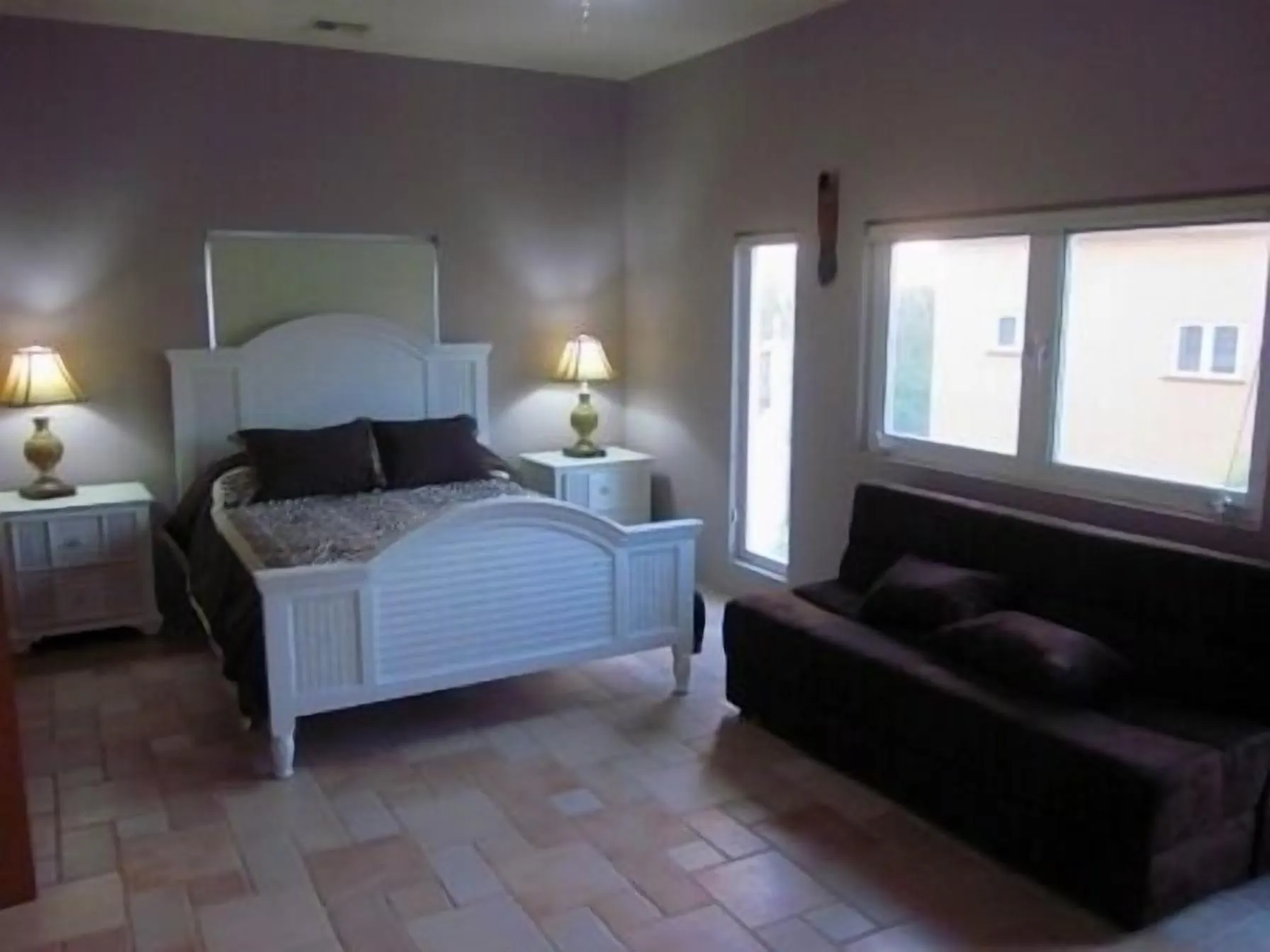 Queen bedroom with bedside tables, a window and a sofa along the far wall