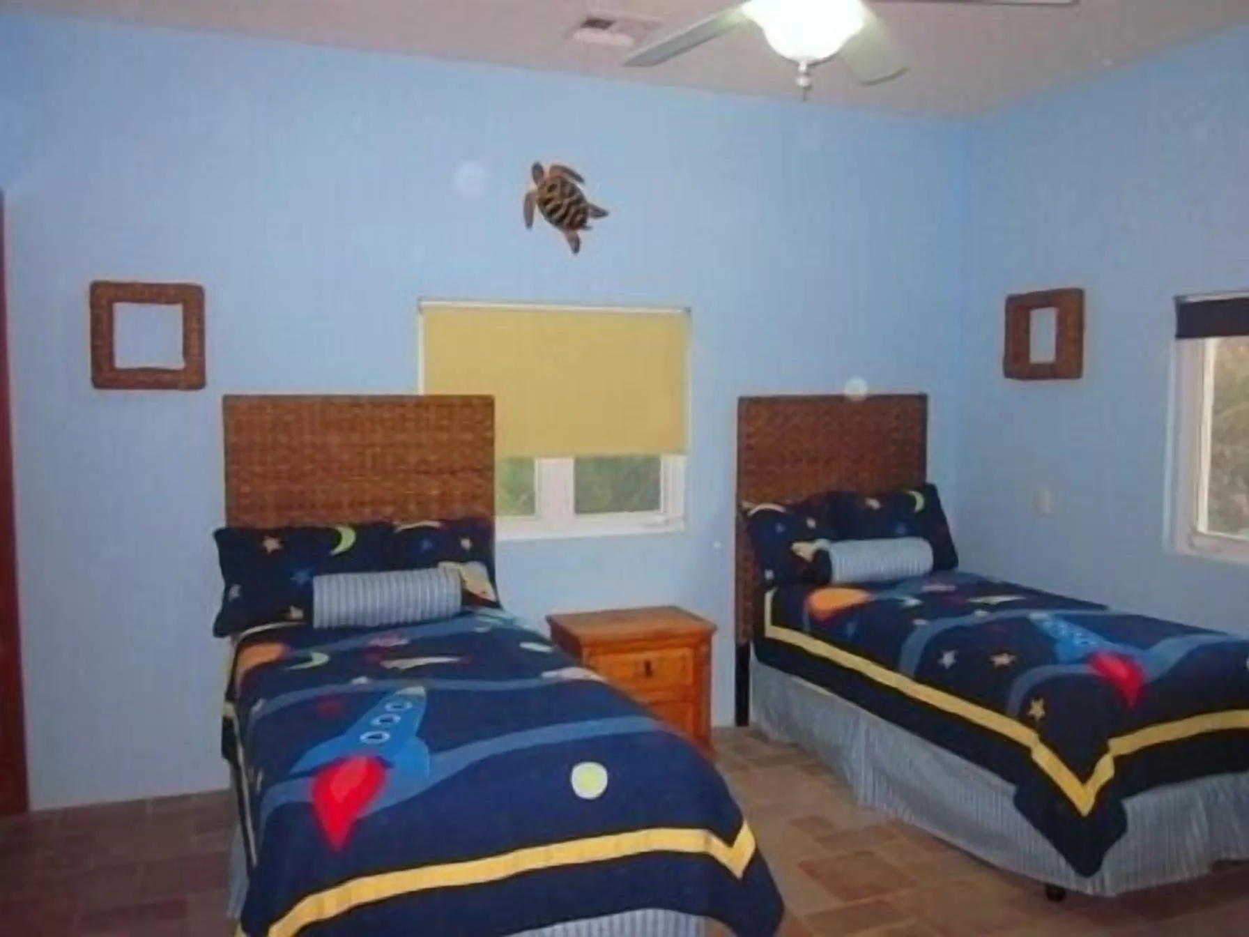 Two twin beds with carved wooden headboards below a window, with a wall light fixture