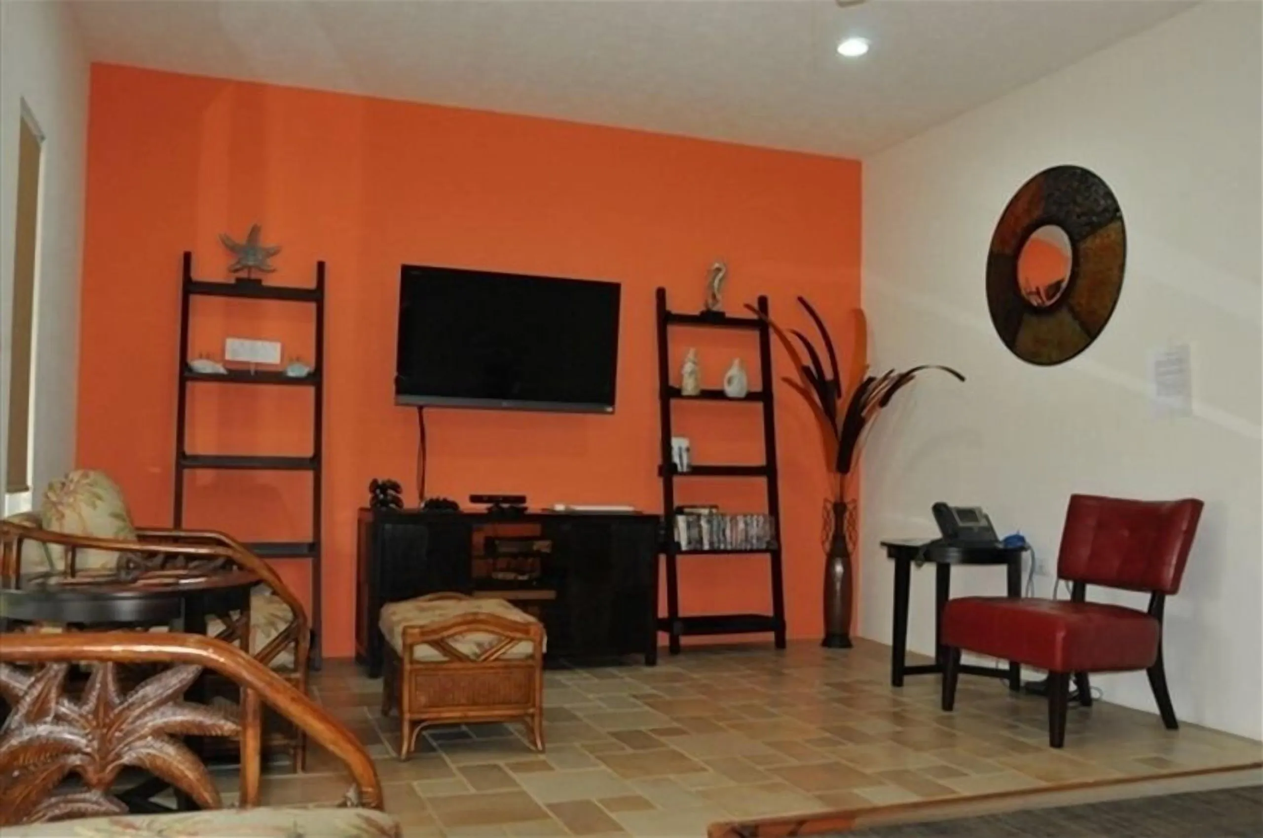 Warm orange-walled sitting room with a flat-screen TV, wooden shelves, a red chair and a large plant