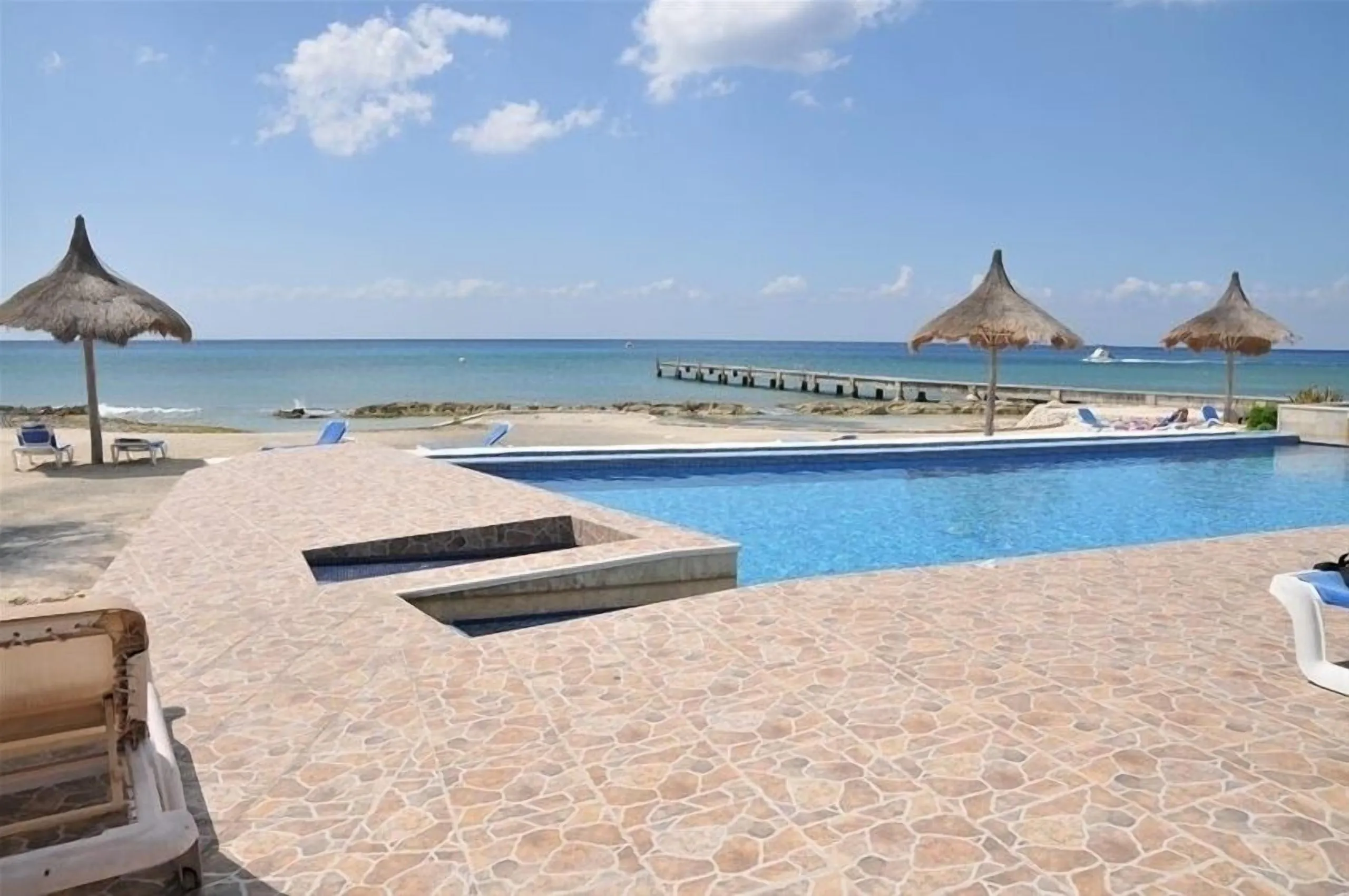 Heated infinity pool at Casa Dana with sun loungers, thatched umbrellas and the private pier running out into the Caribbean