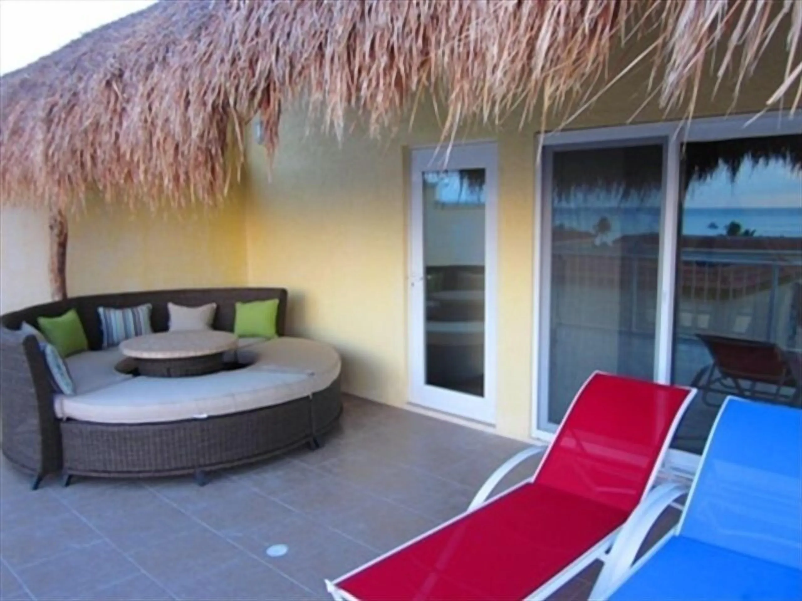 Circular cushioned outdoor seating nook under a thatched roof beside sliding doors to the balcony