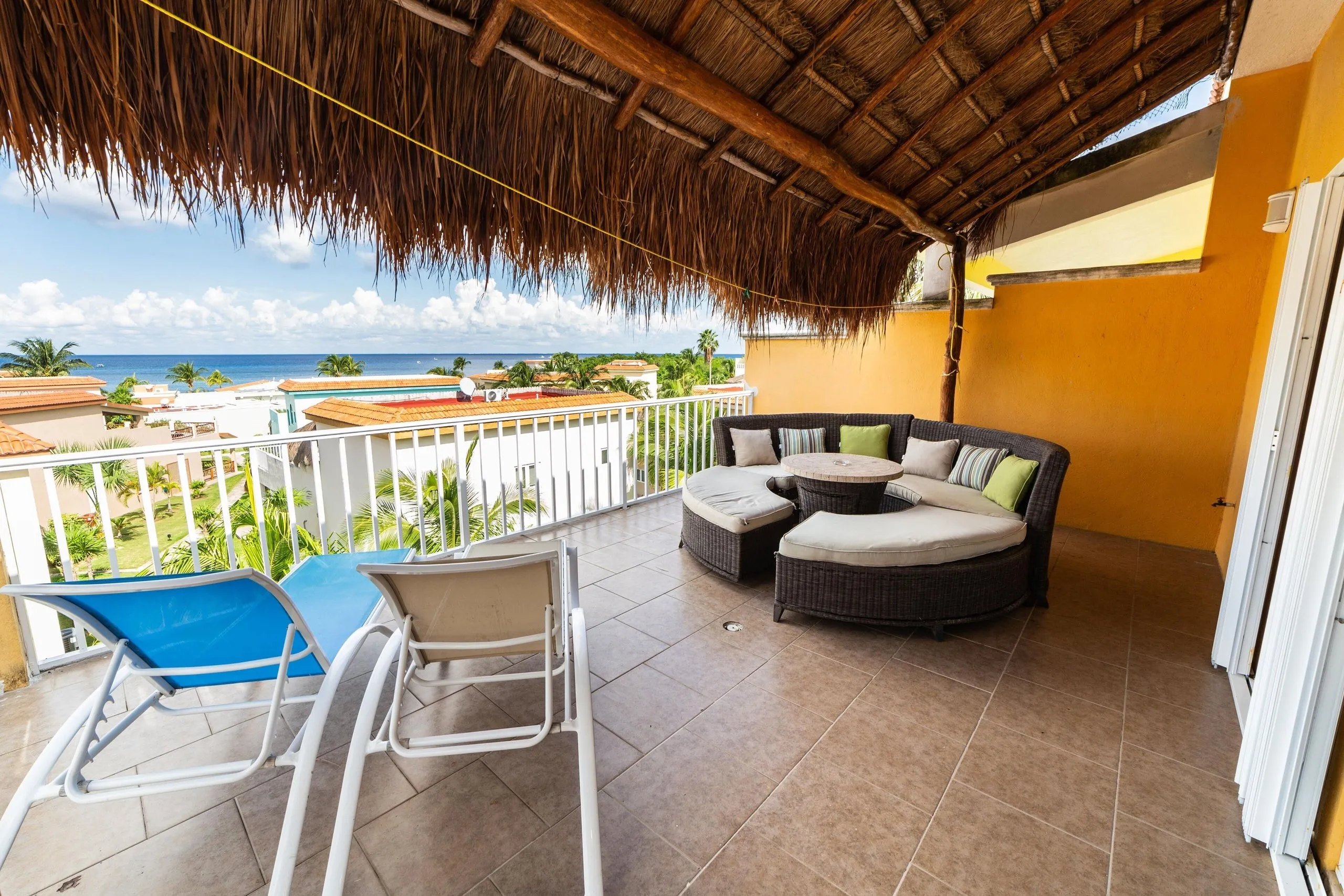 Third-floor terrace at Casa Dana under a thatched palapa roof with wicker furniture and an open view of the ocean