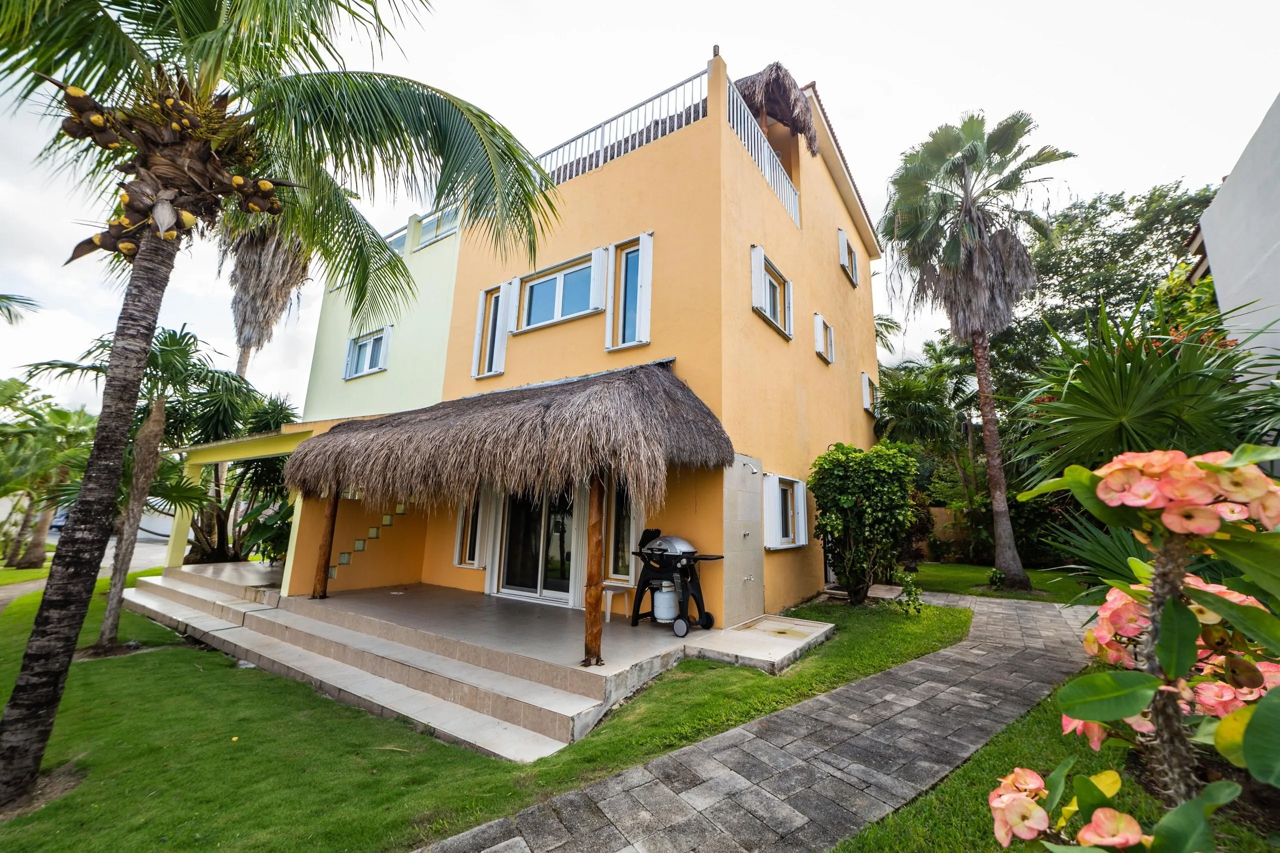 Side of the villa with the outdoor grill and a paved path leading toward the pool area