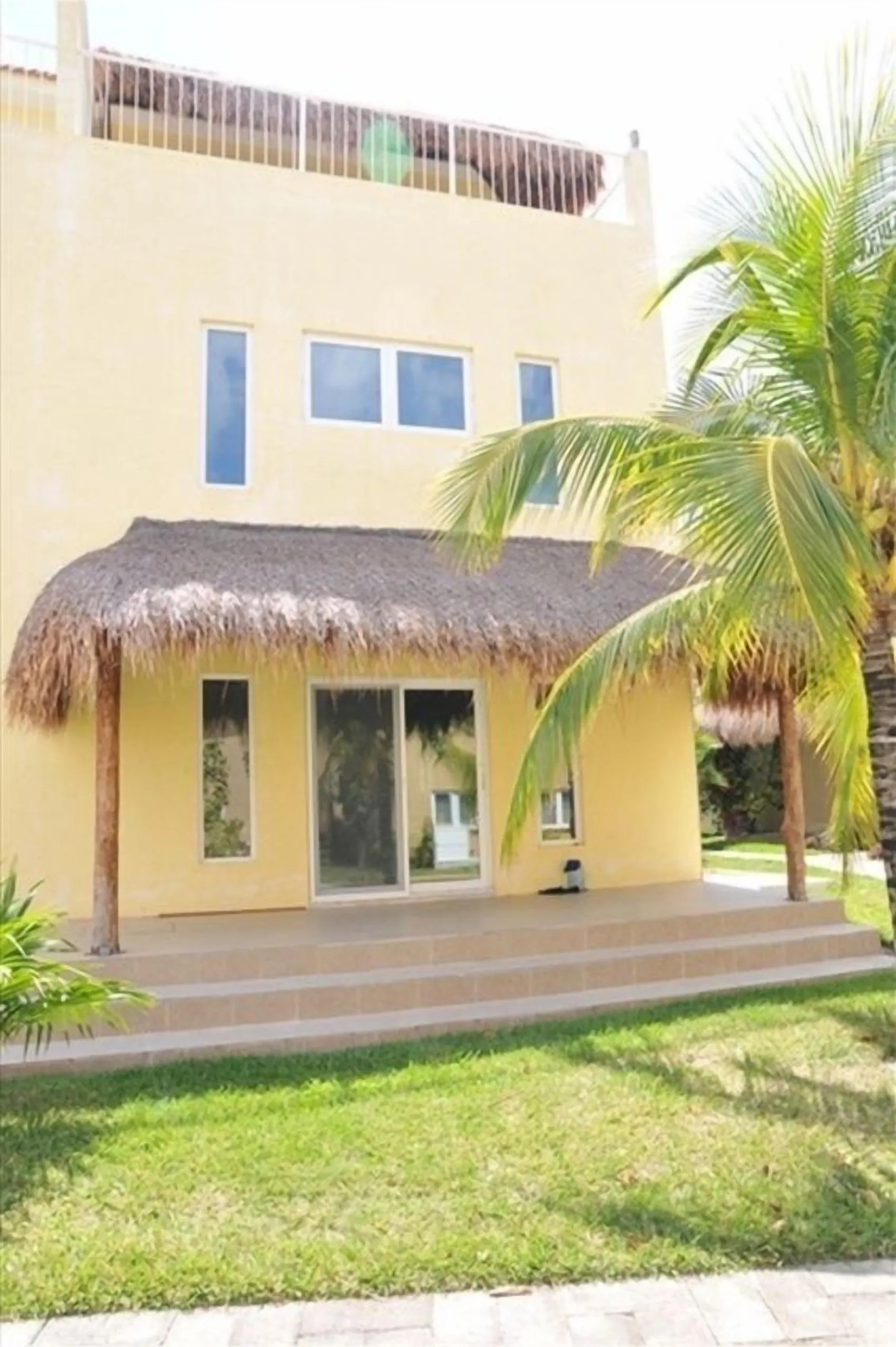 Exterior of the three-story Casa Dana villa with a thatched palapa structure in front and a palm tree beside it